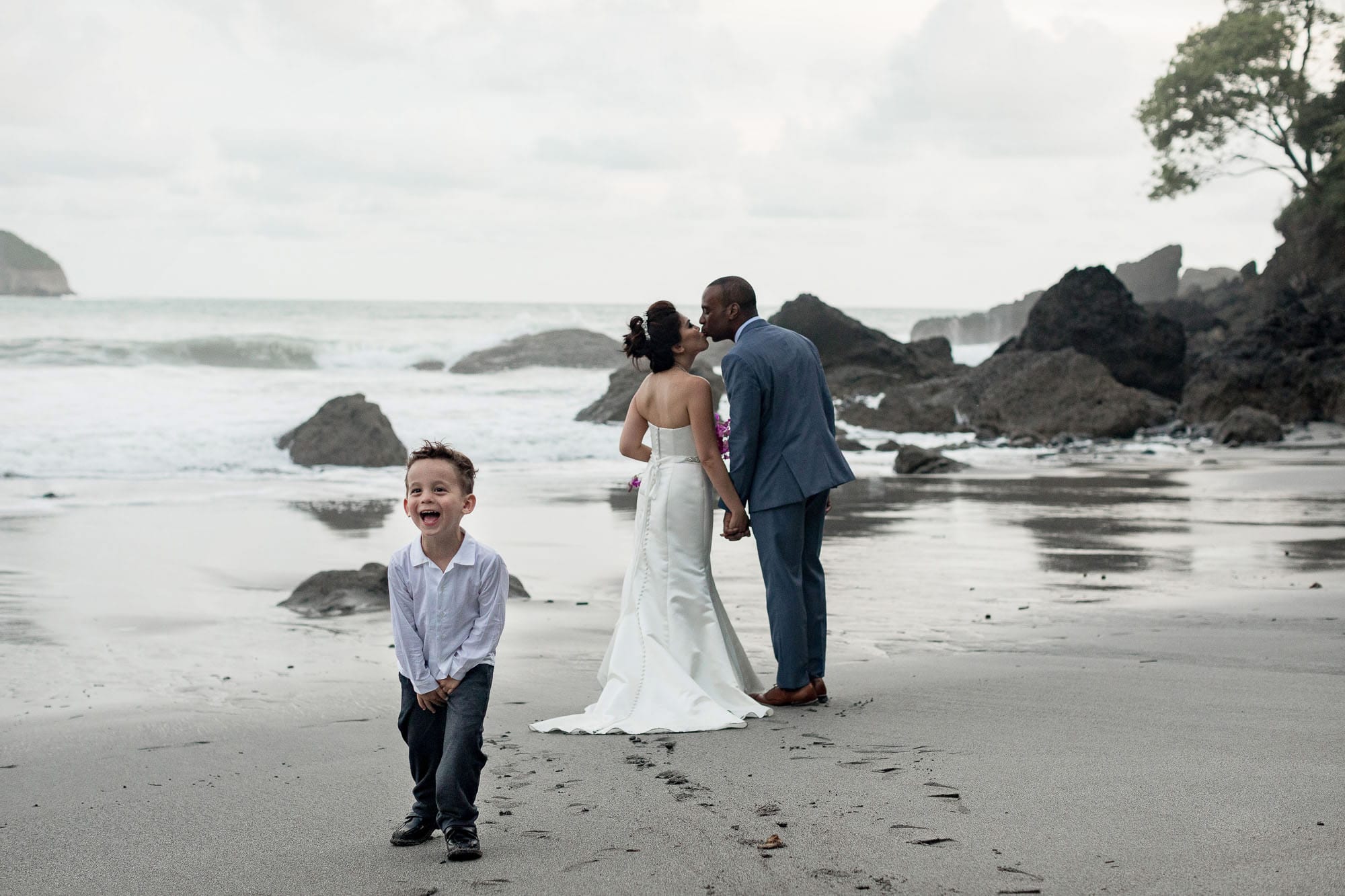 The bride and groom sneak a kiss on the beach and scandalize a little wedding guest!