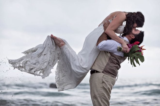 Groom tosses bride in the air as ocean water trickles off her toes