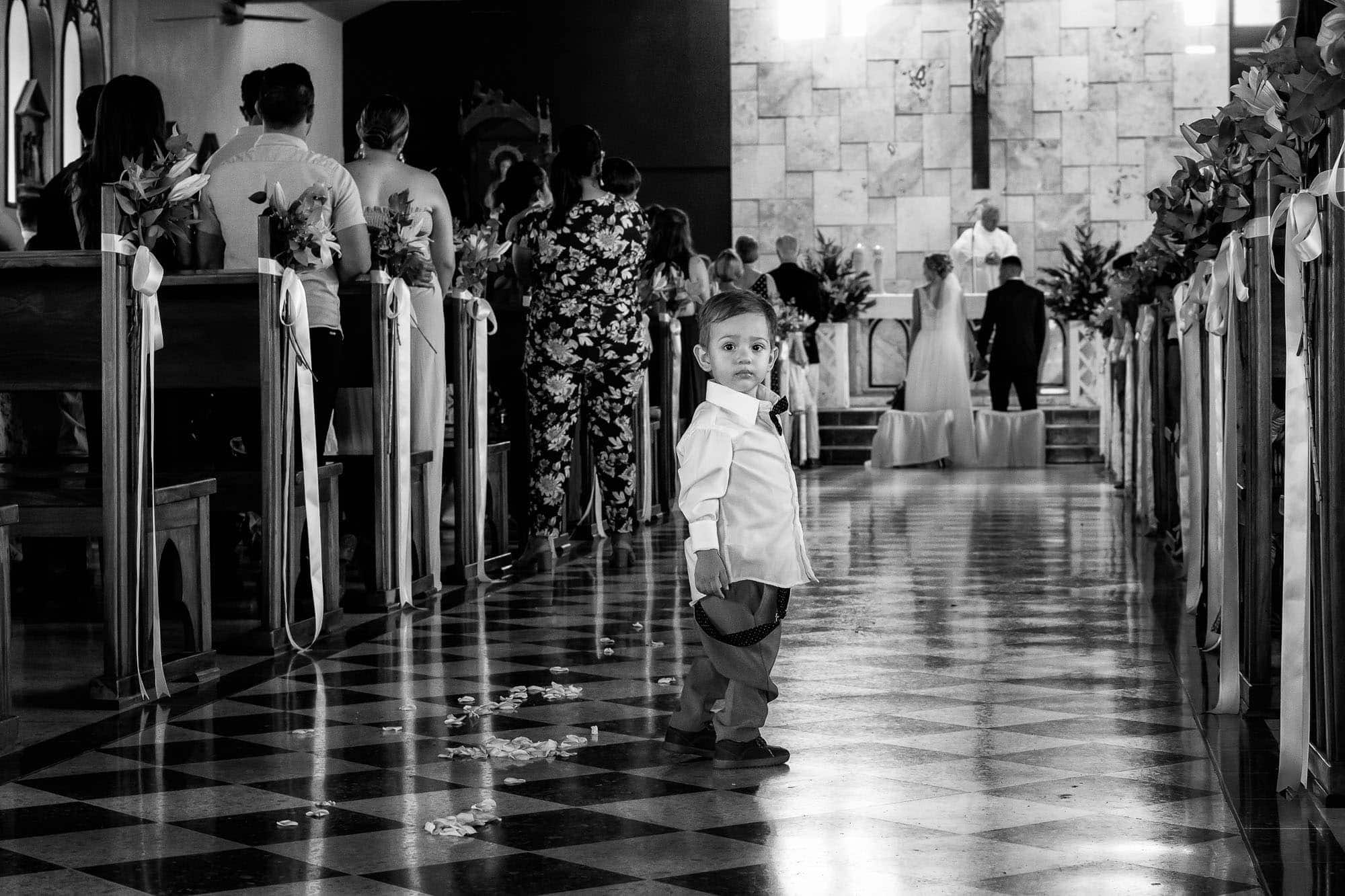 A little boy stands in the aisle behind the bride and groom