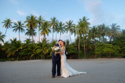 Bride and groom on the beach in front of a line of palms