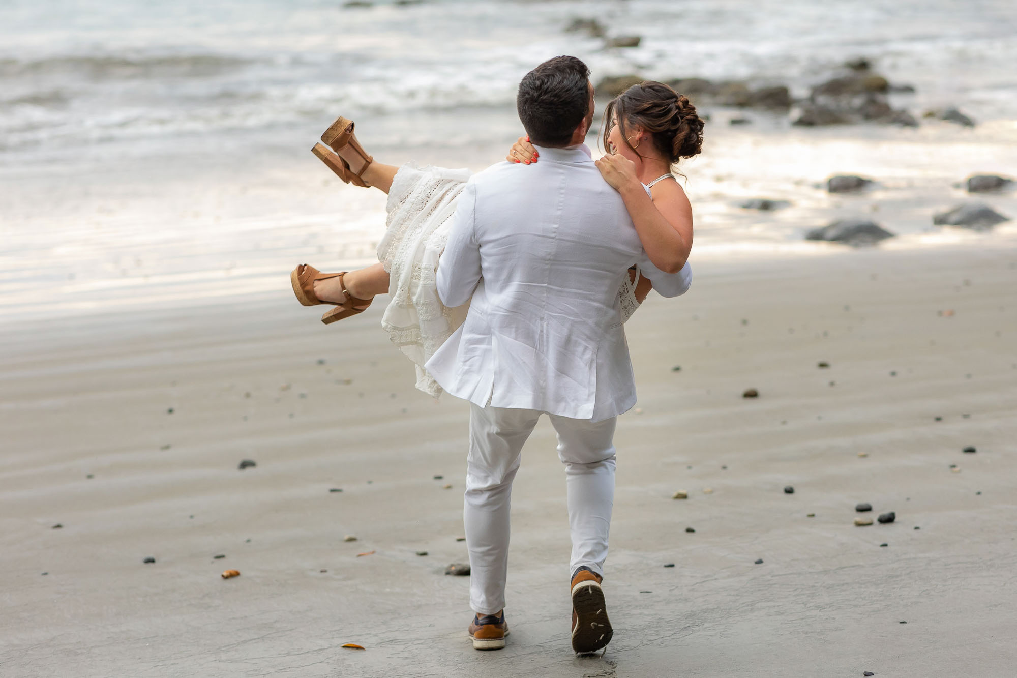 The groom carries his bride off toward the ocean