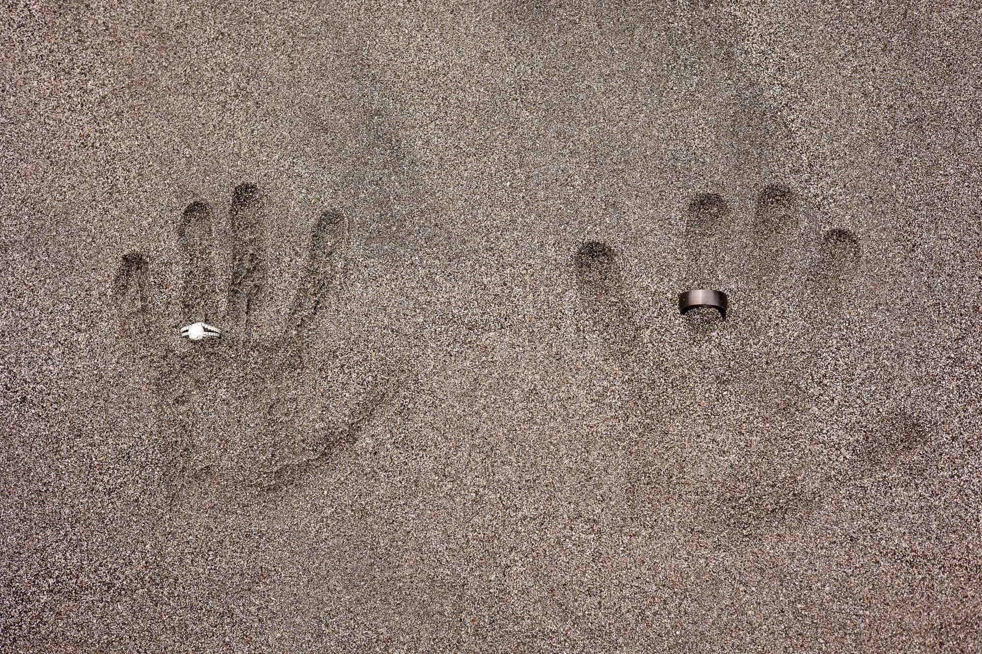 handprints in the sand wearing wedding rings