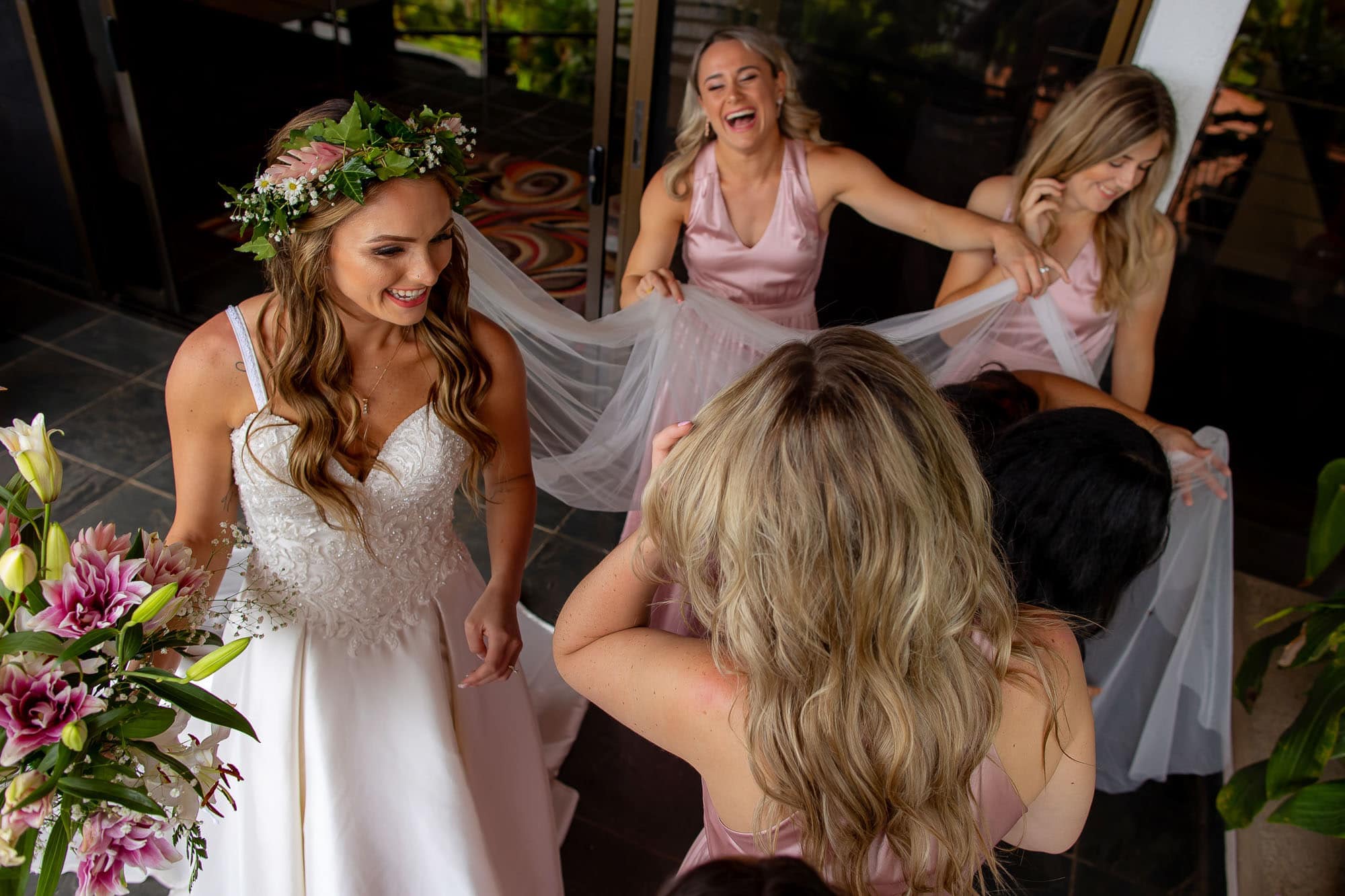 Bridesmaids laughing as they help the bride finish up