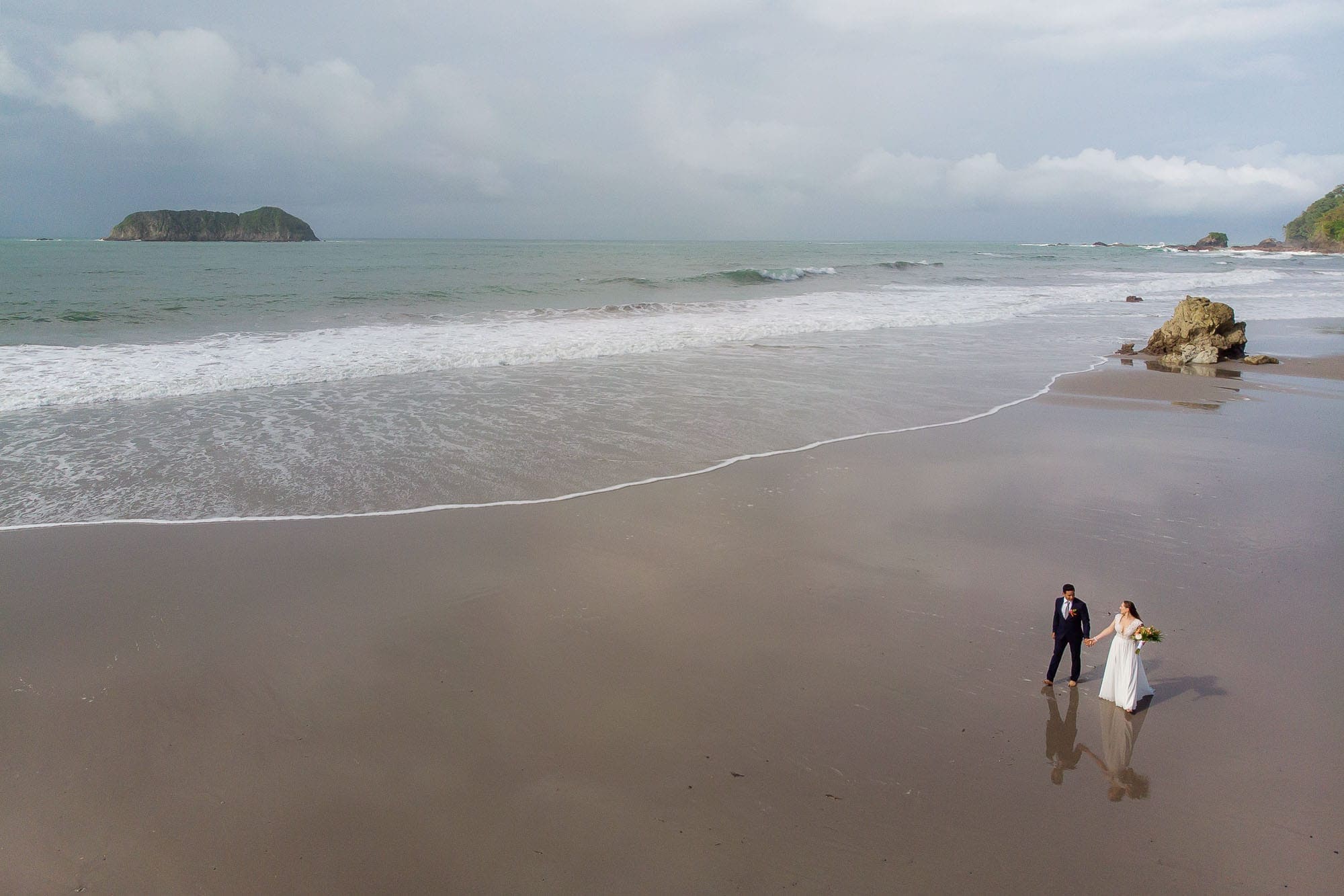 Aerial drone shot of the bride and groom walking along the beach