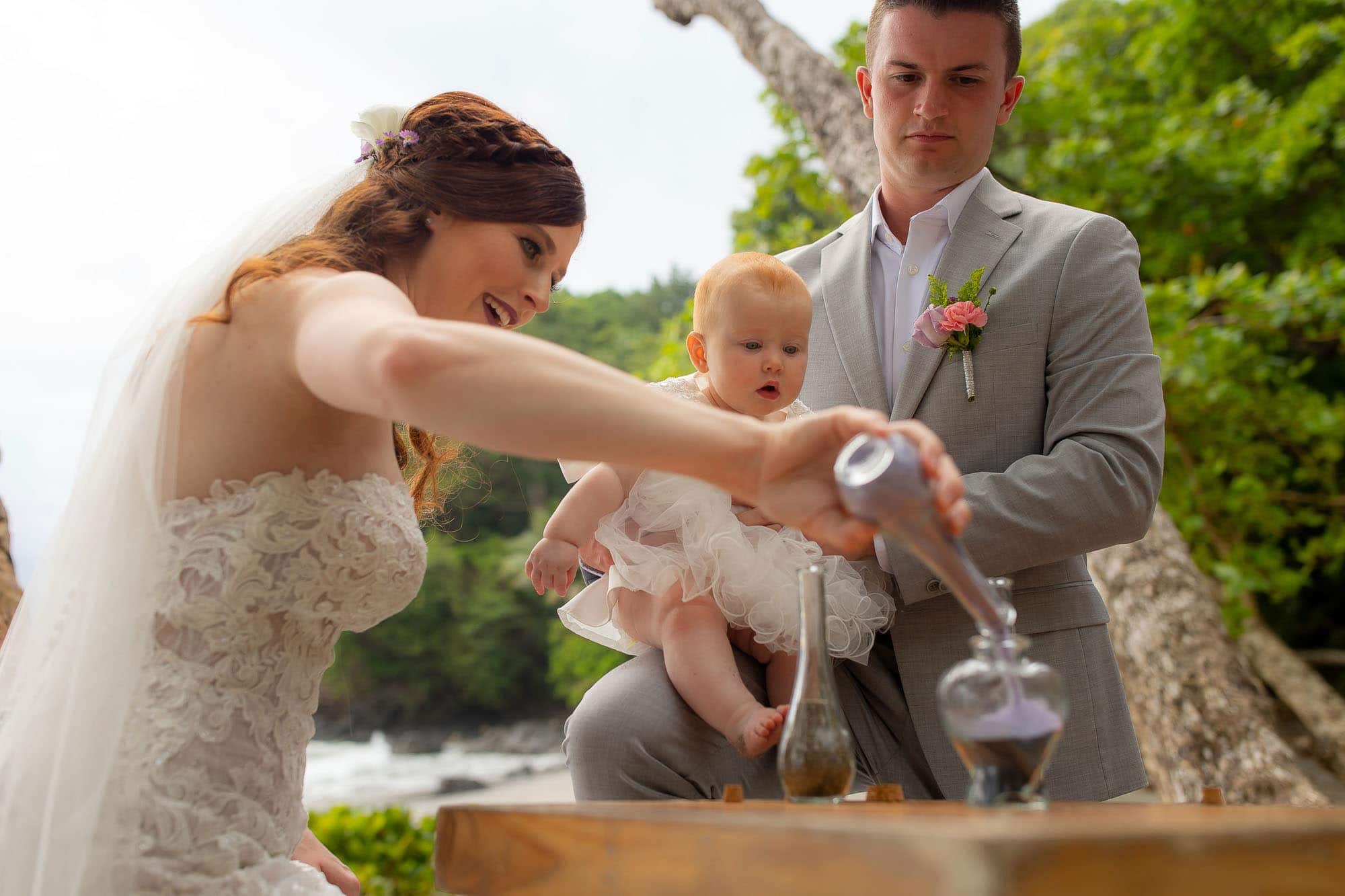 Bride pouring unity sand while groom and baby look on