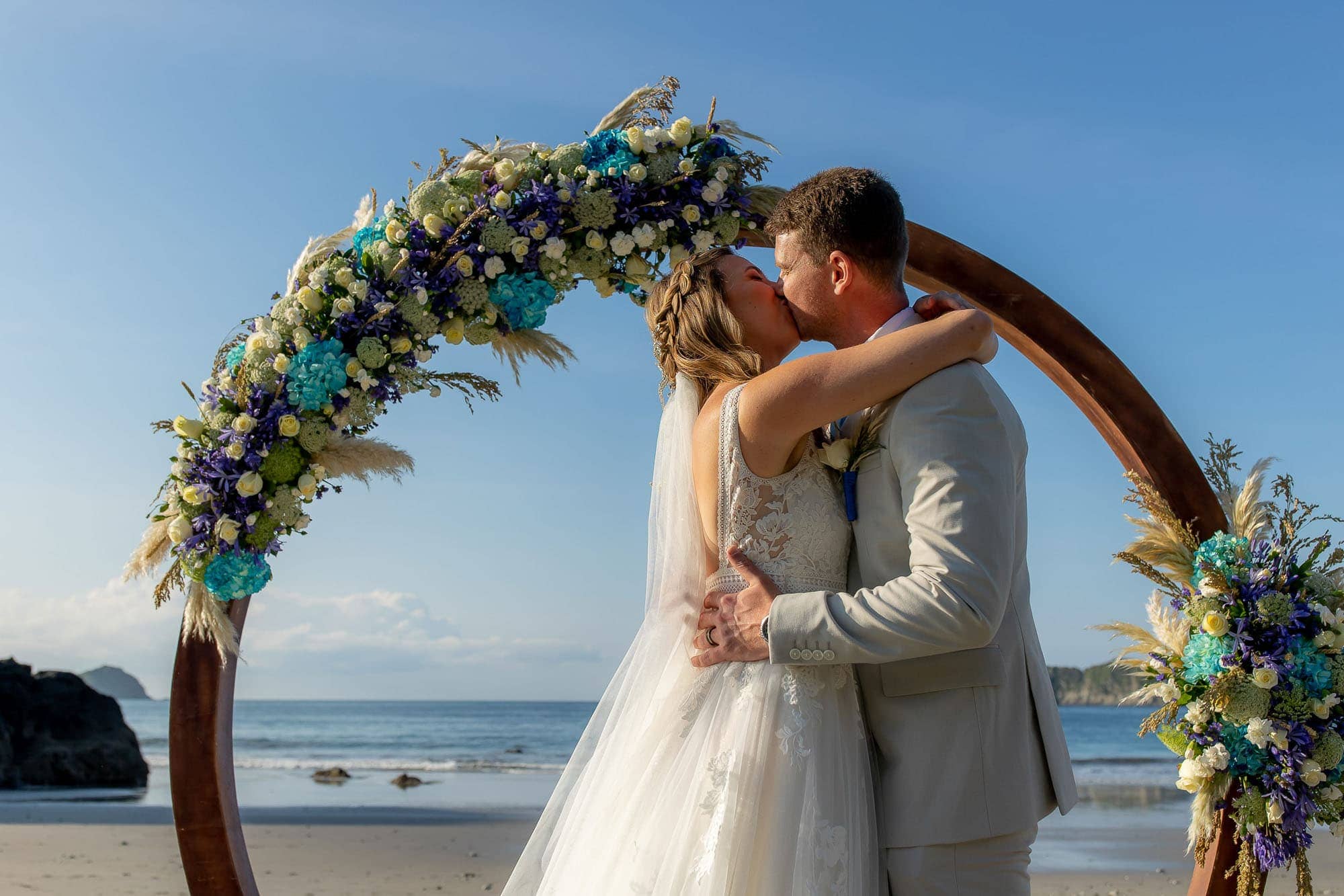 Bride and groom kissing on the beach in front of a circular arbor