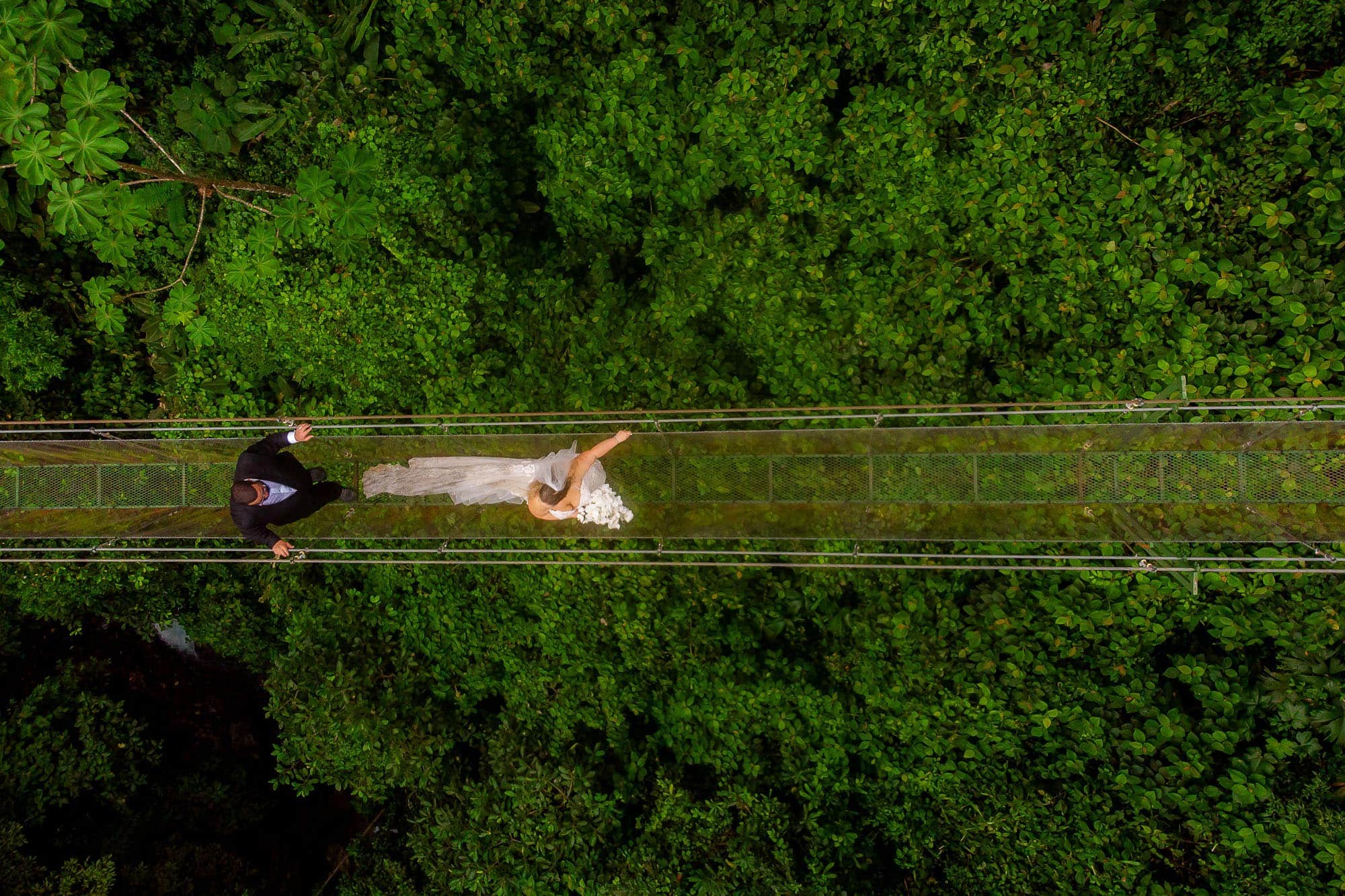 Bride and groom cross the hanging bridge above the waterfall