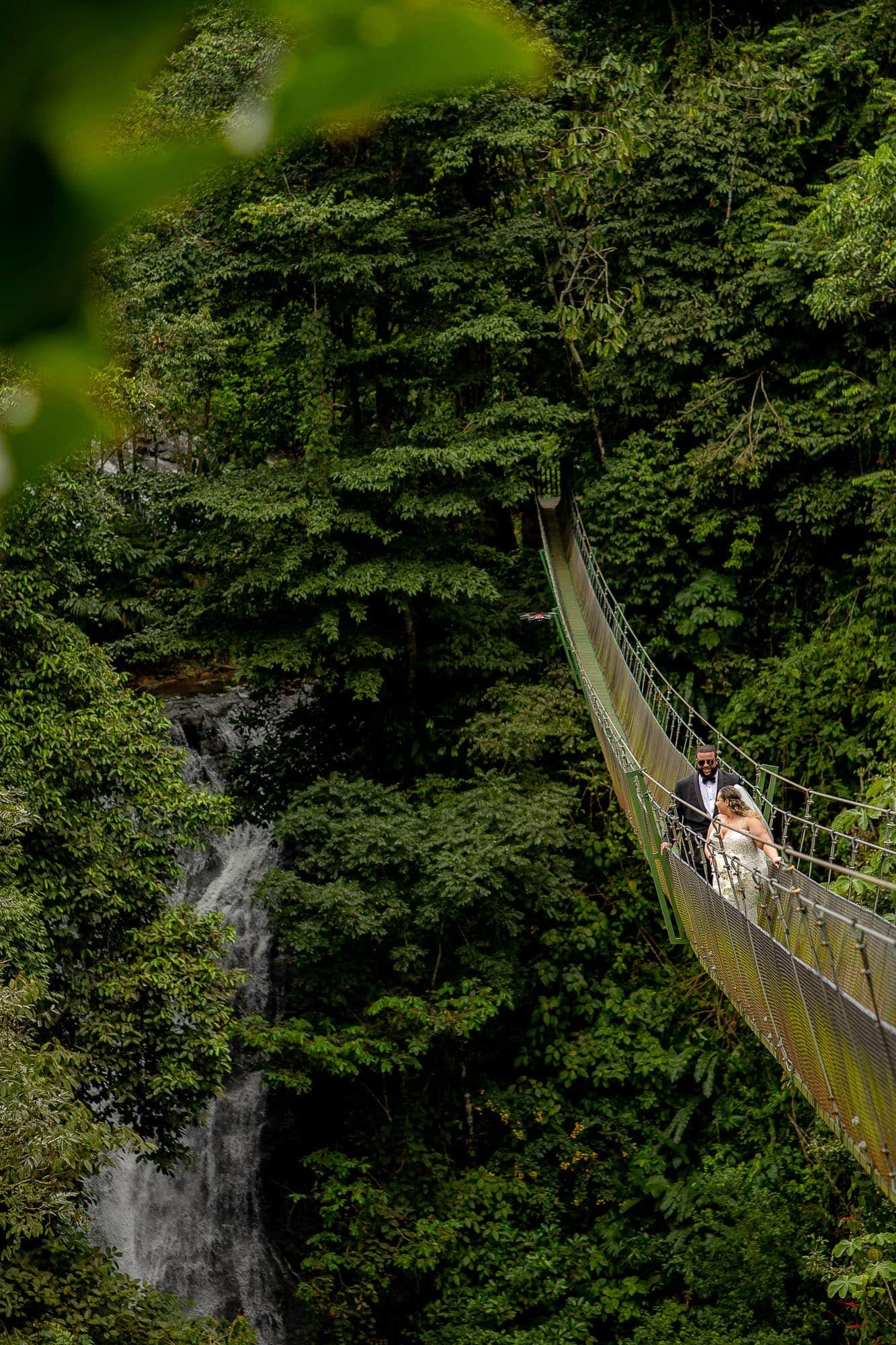 Bride and groom cross the hanging bridge above the waterfall