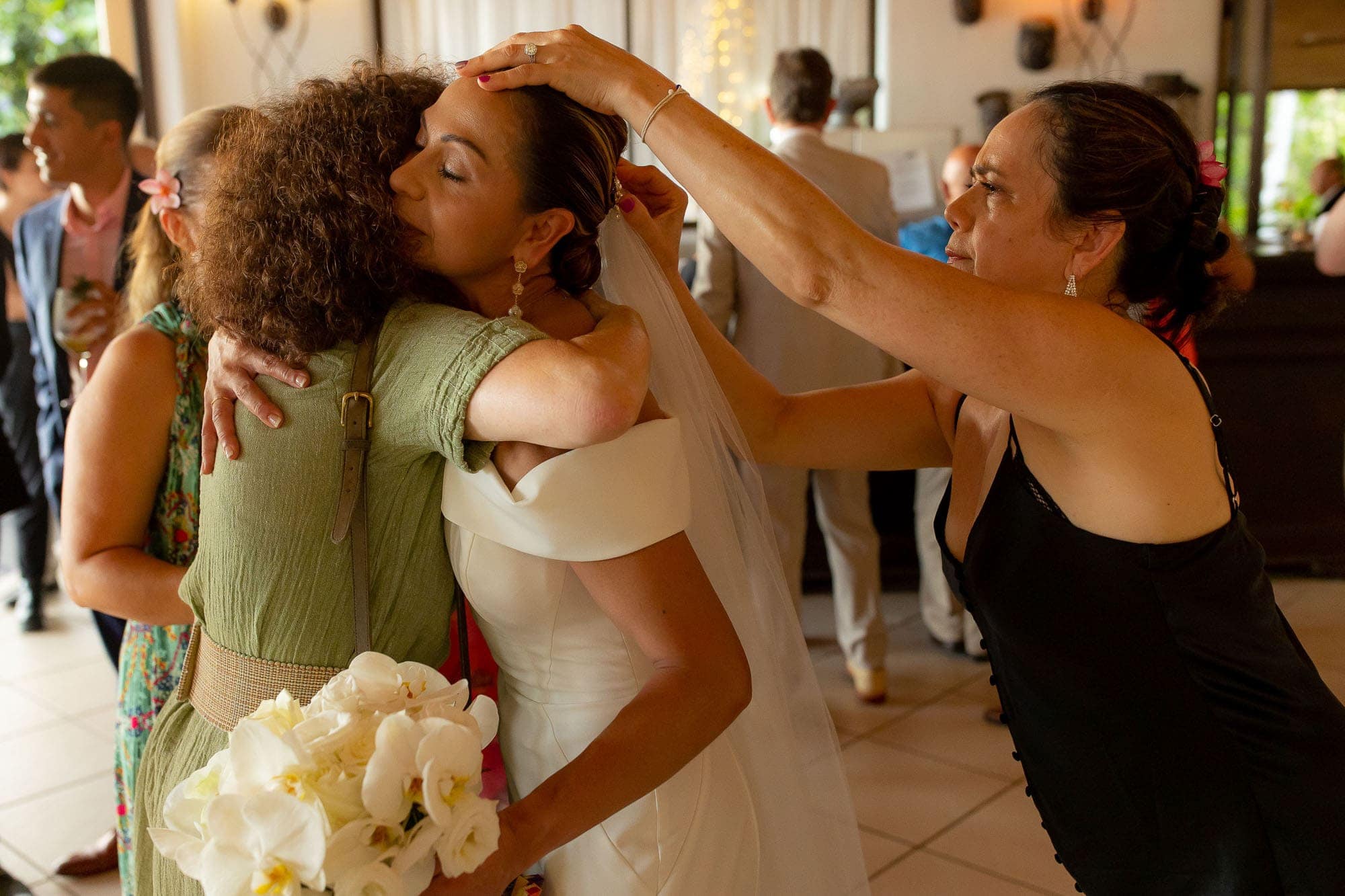bride hugging a guests while another adjusts her veil