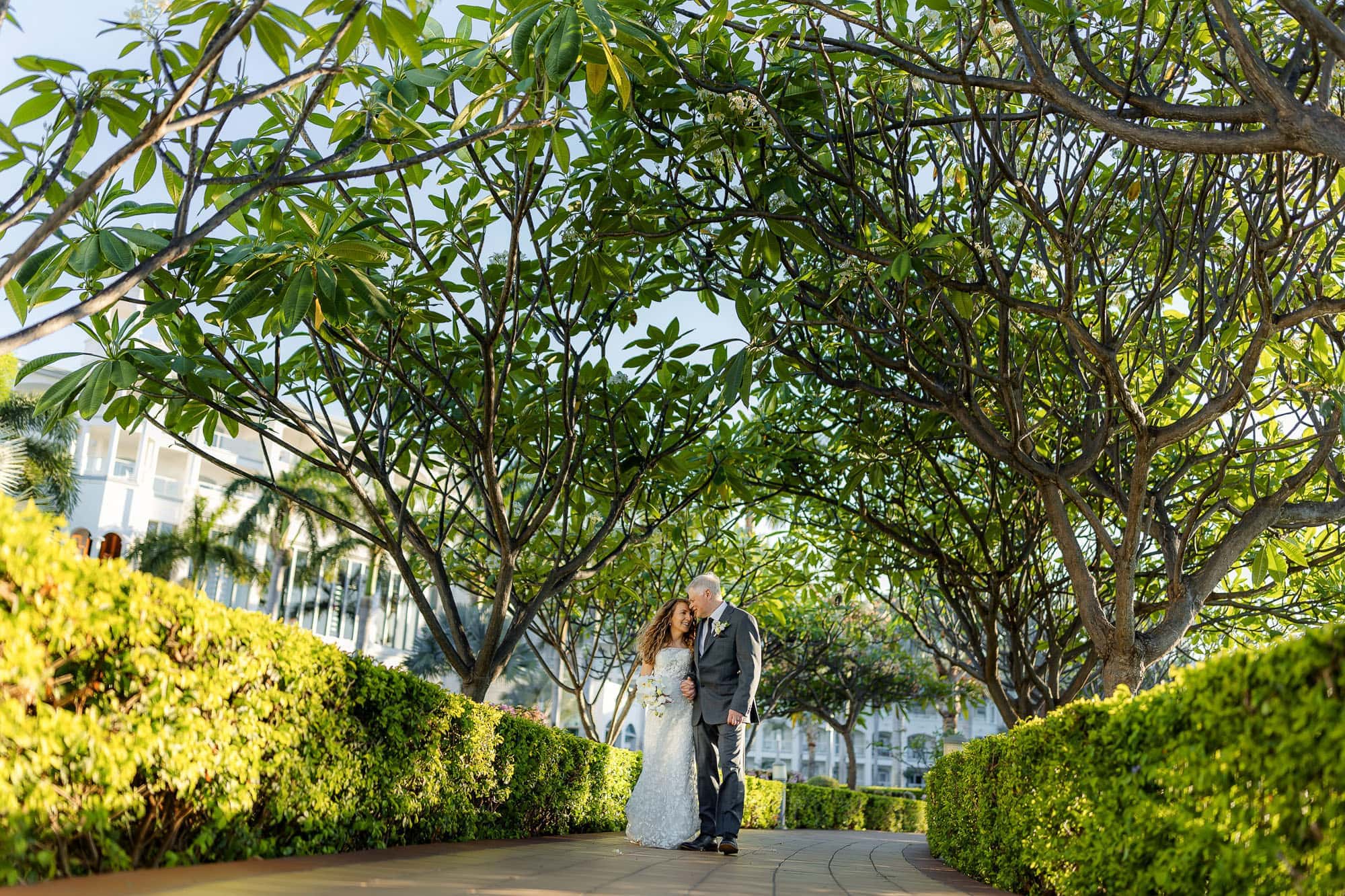 bride and groom stroll along a shaded path at Riu guanacaste